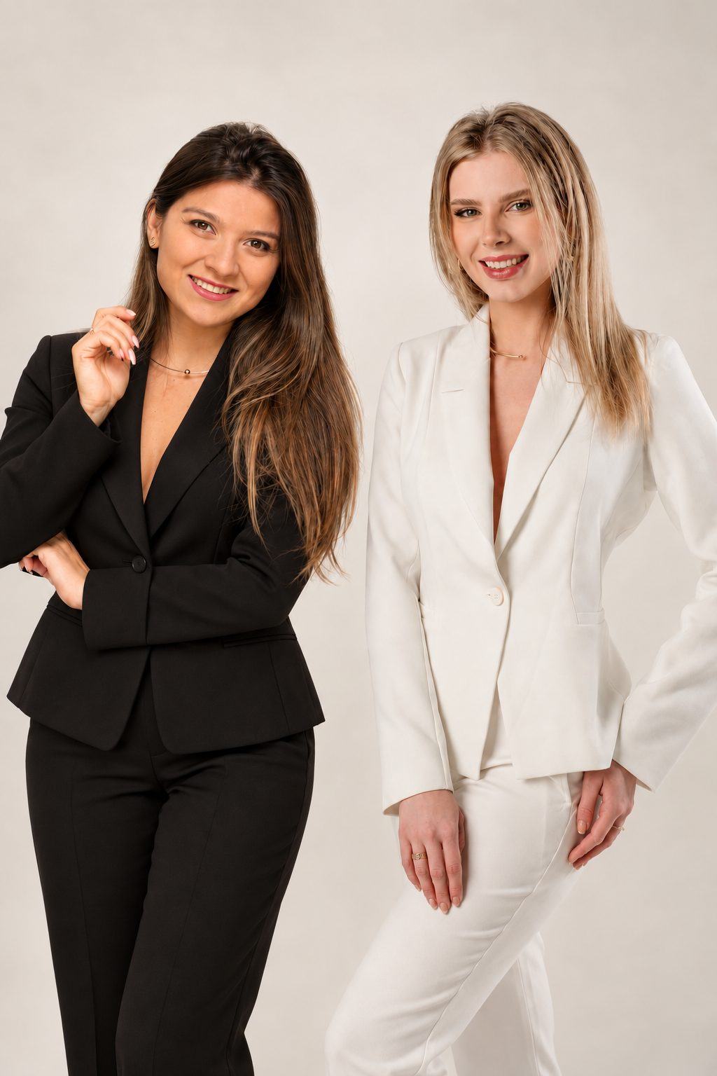 Chiara e Mayara juntas, sorrindo, uma de terno preto e outra de terno branco